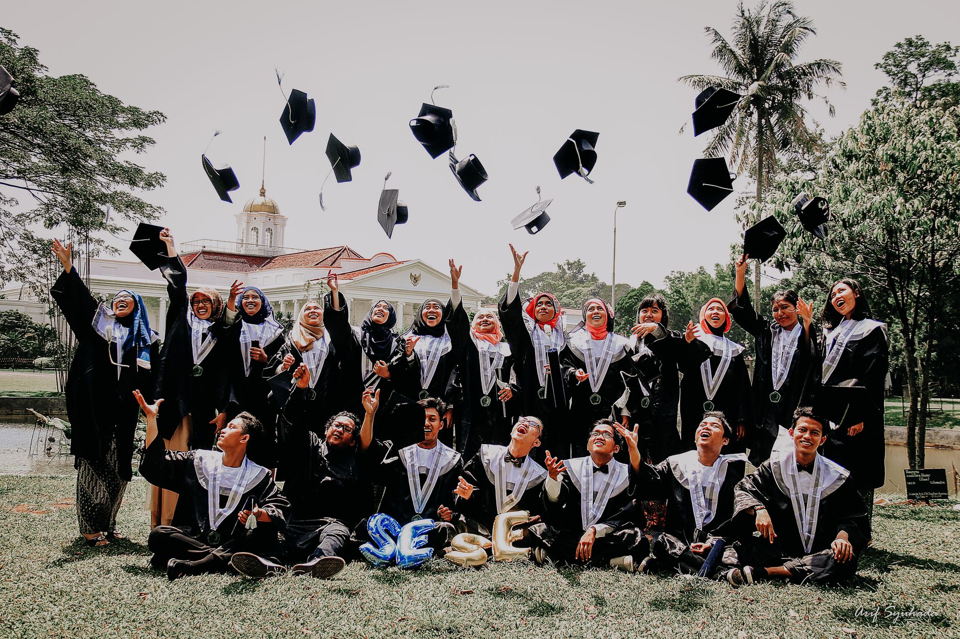 A joyful group of graduates celebrating outdoors, tossing caps in the air.