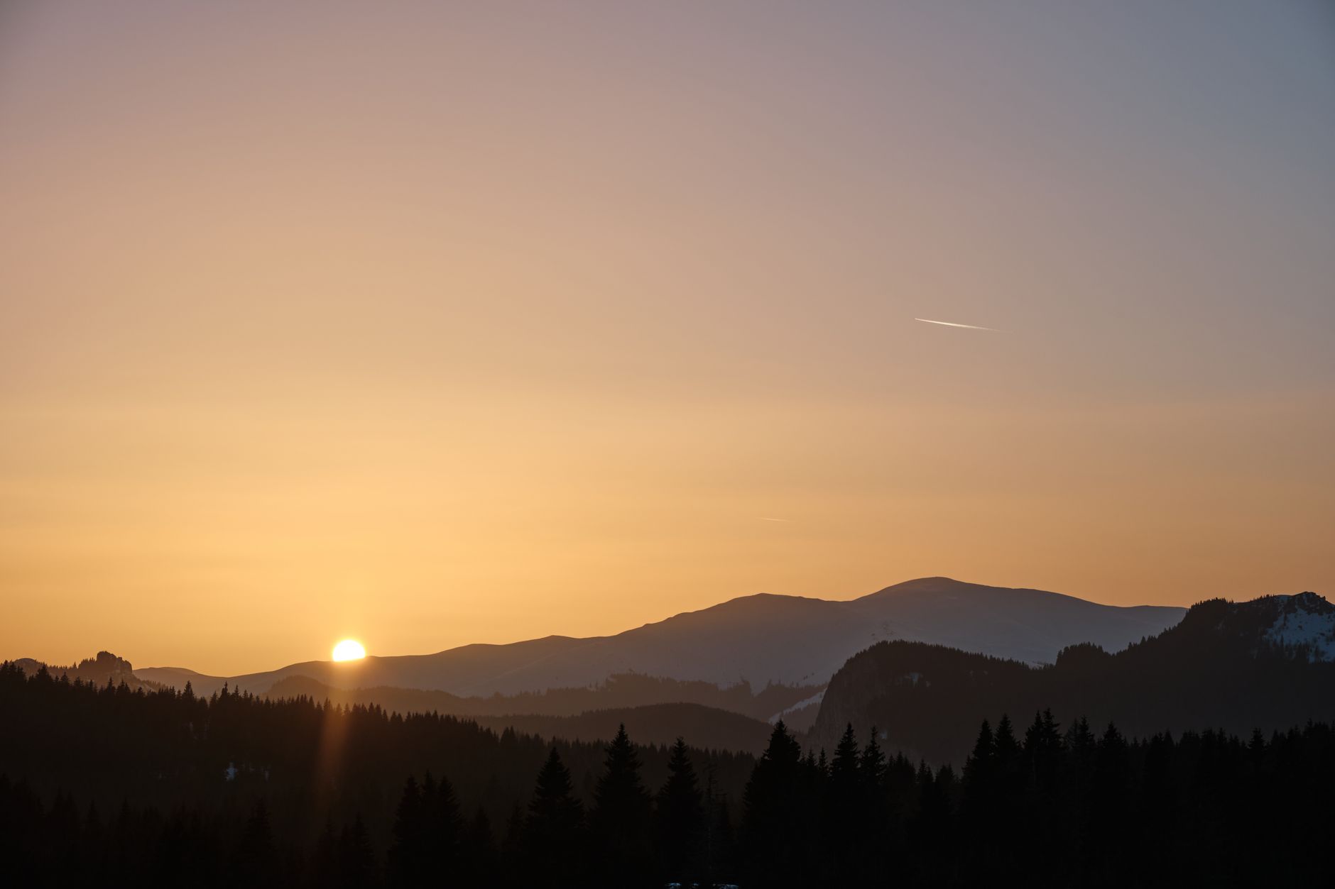 Beautiful sunset over mountains with silhouetted trees and a clear sky.