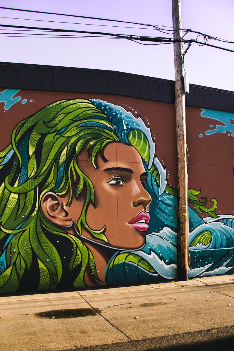 Colorful street art mural depicting a woman with flowing green hair on an urban wall.