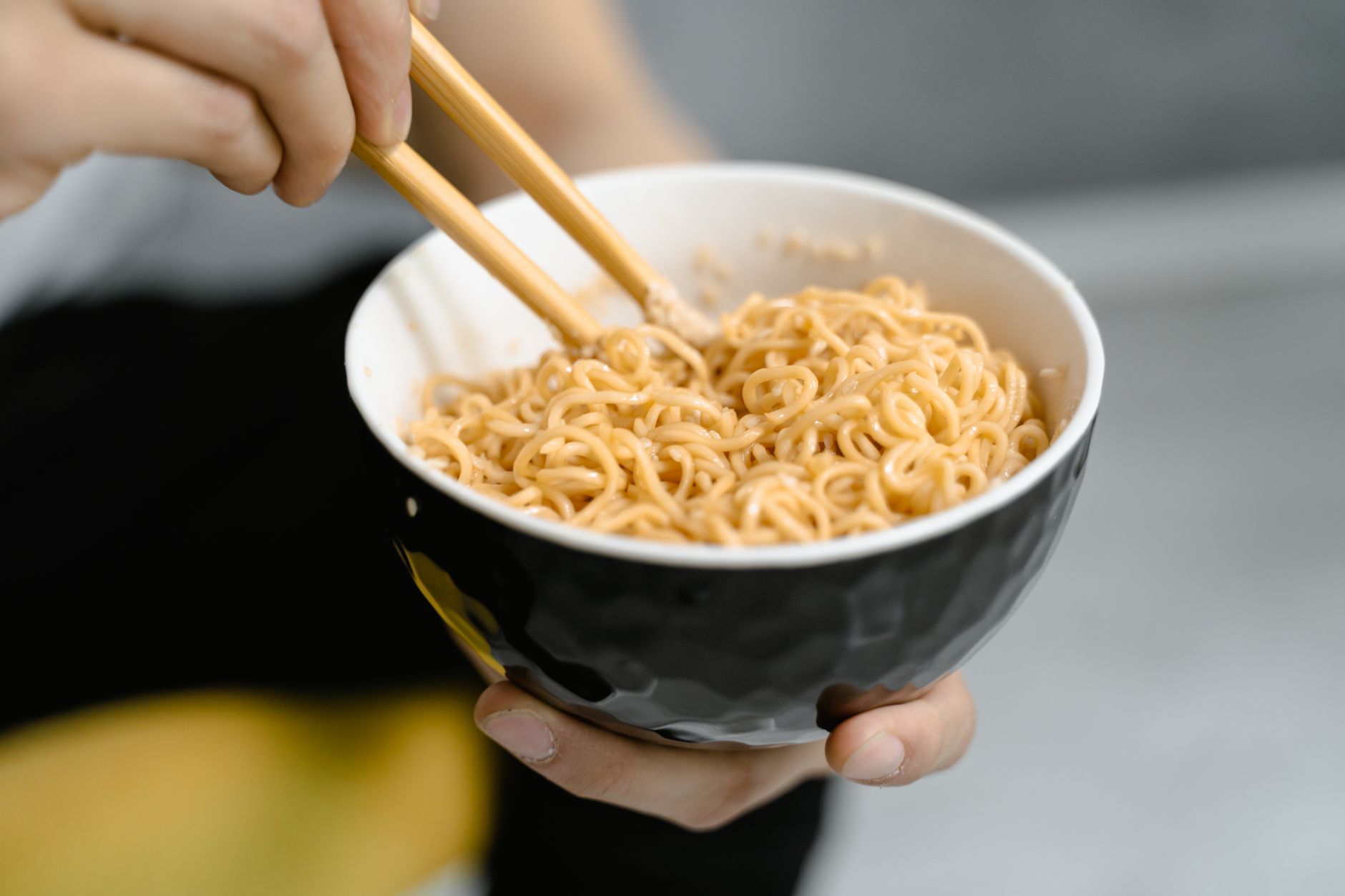 A person holding a bowl of noodles with chopsticks, captured in a close-up shot.