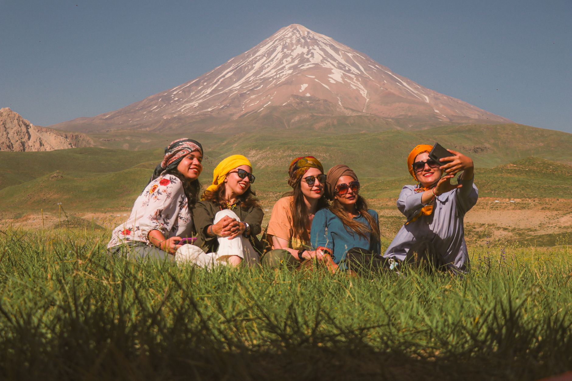 Group of friends enjoying a sunny day, taking a selfie with a mountain backdrop.
